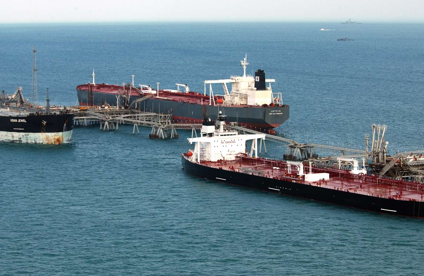 Three crude oil tankers moored at the loading arms of an offshore oil terminal in open Gulf water, seen from above. Pipework runs from the terminal platform to each vessel.